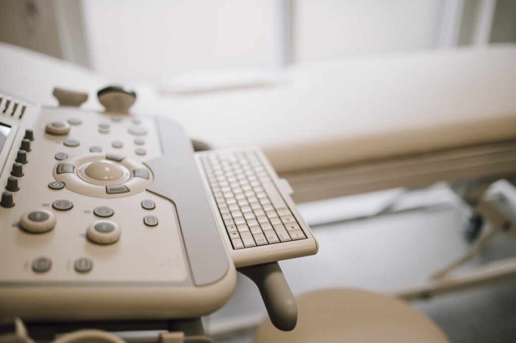 Console d'un échographe en salle d'examen : gros plan sur les molettes, boutons et trackball utilisés en pratique clinique