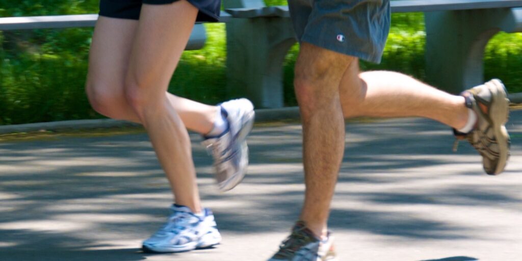 Jambes de deux joggeurs en foulée sur une allée de parc, genoux fléchis, flou de mouvement