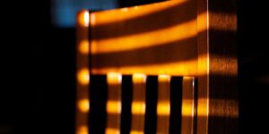 Rayures de lumière et d'ombre projetées sur le dossier en bois d'une chaise, lignes parallèles sur fond sombre
